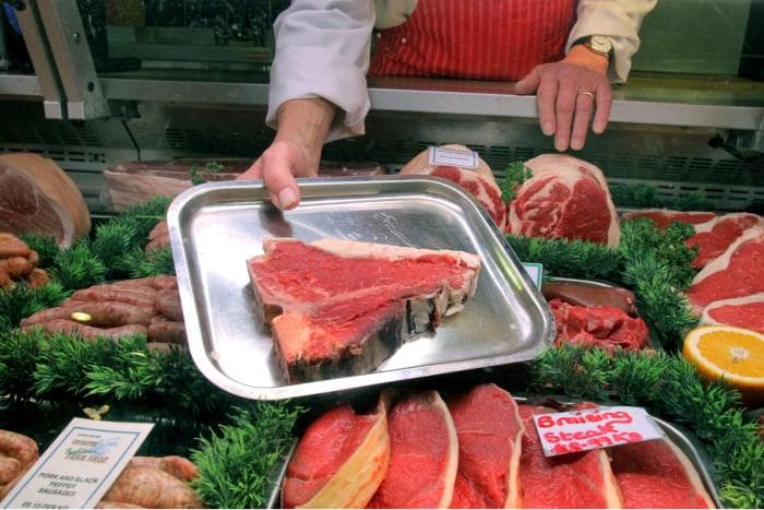 A Churston butcher presenting a T-bone steak over the counter, surrounded by sausages and steaks