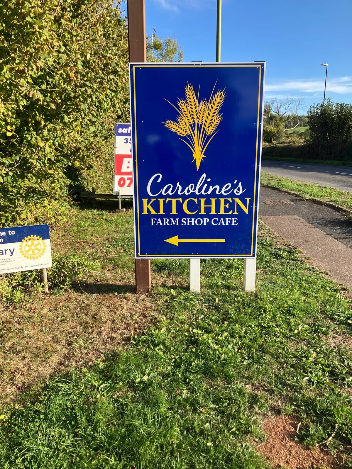 The blue and gold Caroline's Kitchen farm shop café sign by the Dartmouth Road, pointing the way in