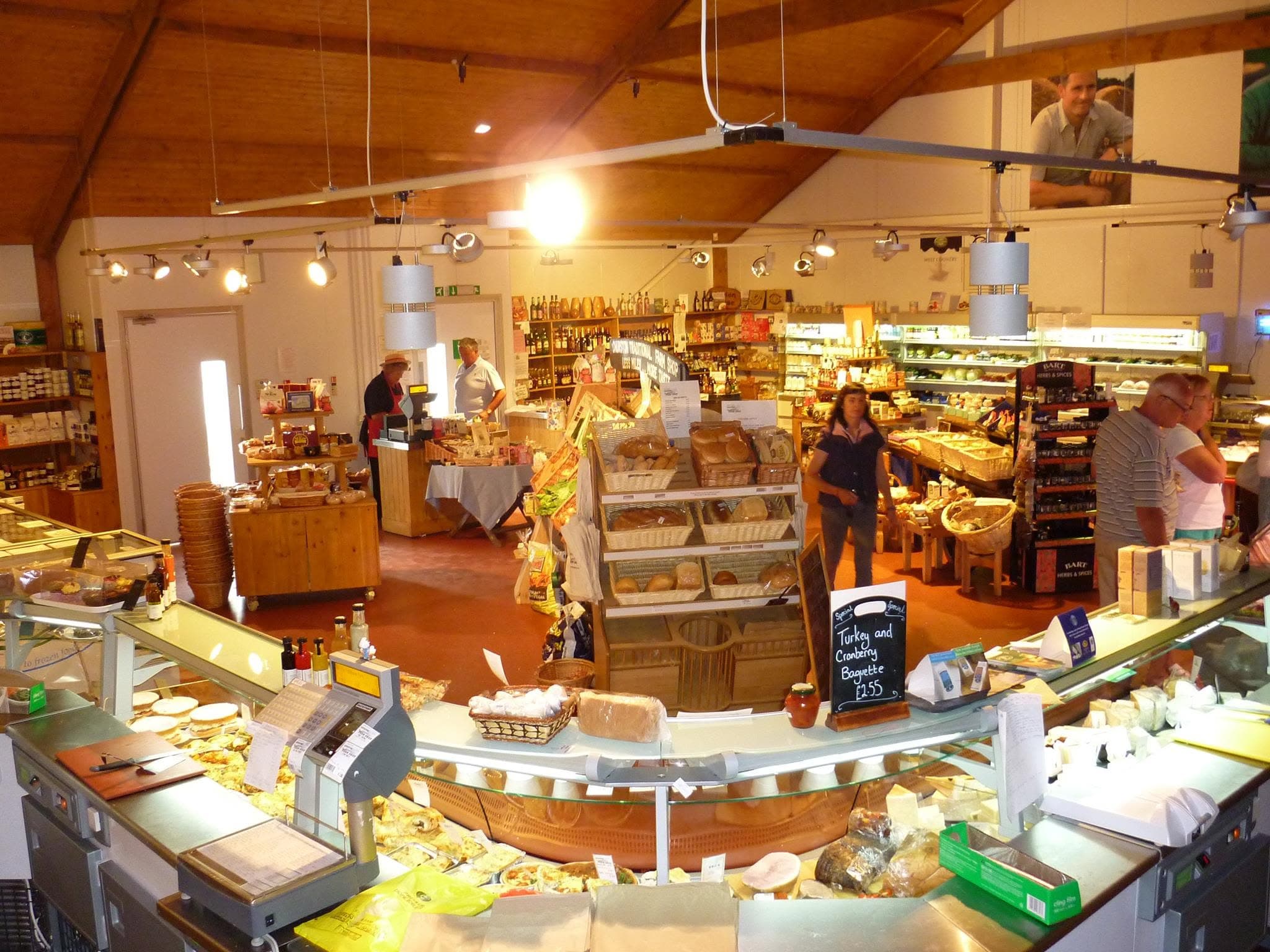 The Churston shop floor — bread baskets beside the deli counter, shelves of West Country produce under the timber roof