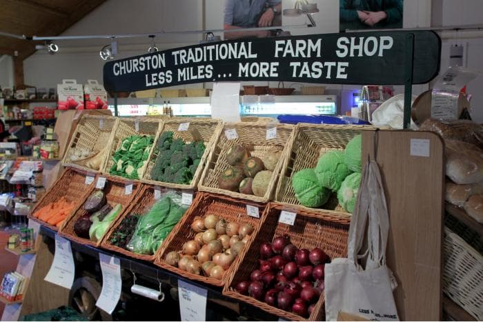 Baskets of local vegetables under the Churston Traditional Farm Shop sign — less miles, more taste